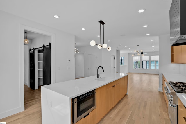 kitchen with light hardwood / wood-style flooring, a spacious island, sink, a barn door, and high end stove