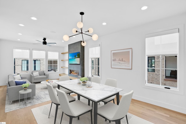 dining space with a fireplace, ceiling fan with notable chandelier, and light wood-type flooring