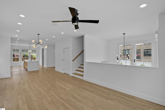 unfurnished living room featuring sink, ceiling fan with notable chandelier, and light hardwood / wood-style flooring