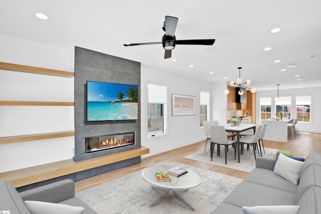 living room with a fireplace, ceiling fan with notable chandelier, and light wood-type flooring