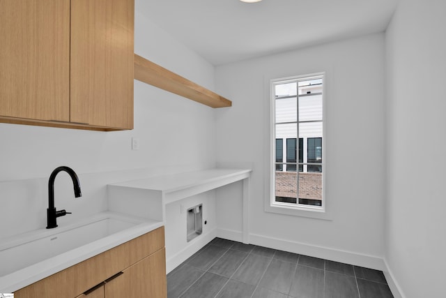 laundry area featuring sink, dark tile patterned floors, a healthy amount of sunlight, and cabinets