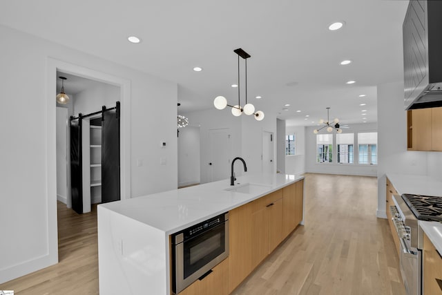 kitchen with stainless steel stove, decorative light fixtures, sink, a large island with sink, and a barn door