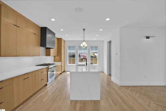 kitchen featuring decorative light fixtures, stainless steel range, light stone counters, a center island with sink, and wall chimney exhaust hood