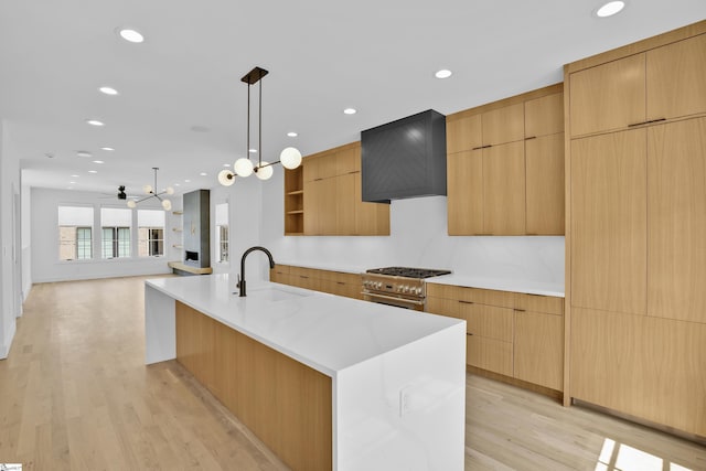 kitchen featuring high end stainless steel range, sink, decorative light fixtures, a large island, and wall chimney range hood