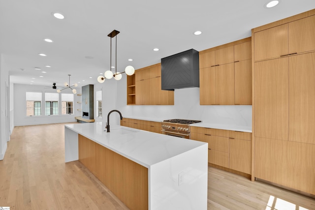 kitchen with sink, stainless steel stove, decorative light fixtures, light wood-type flooring, and premium range hood