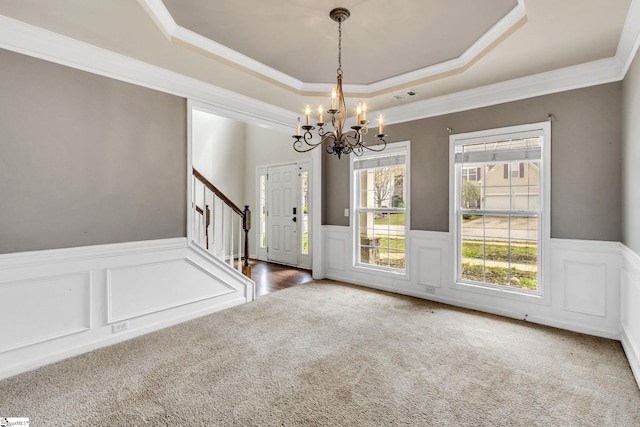 unfurnished dining area with carpet floors, crown molding, a raised ceiling, and a chandelier