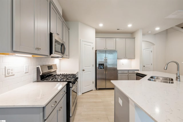 kitchen with sink, stainless steel appliances, decorative backsplash, and light stone countertops