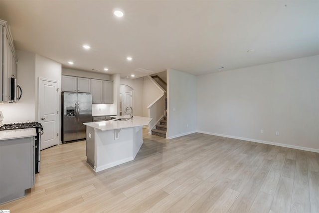 kitchen with a kitchen island with sink, sink, appliances with stainless steel finishes, and light hardwood / wood-style floors