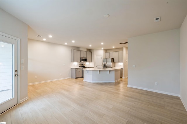 kitchen with a kitchen island with sink, light hardwood / wood-style floors, stainless steel appliances, and gray cabinets