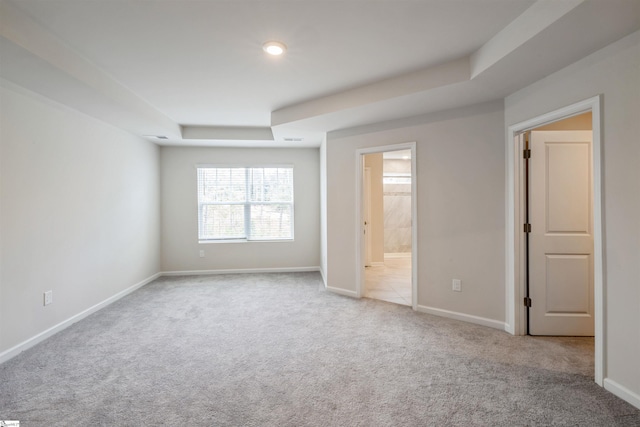 unfurnished bedroom featuring a tray ceiling, light carpet, and ensuite bathroom