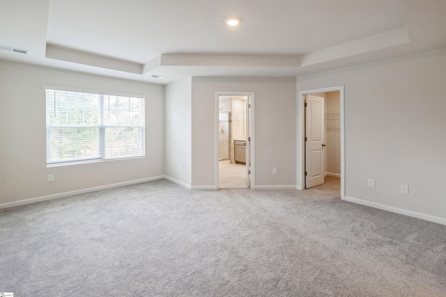 unfurnished bedroom featuring ensuite bath, a closet, a spacious closet, light carpet, and a tray ceiling