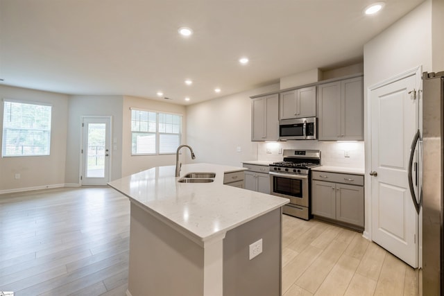 kitchen featuring sink, appliances with stainless steel finishes, light hardwood / wood-style flooring, decorative backsplash, and light stone countertops