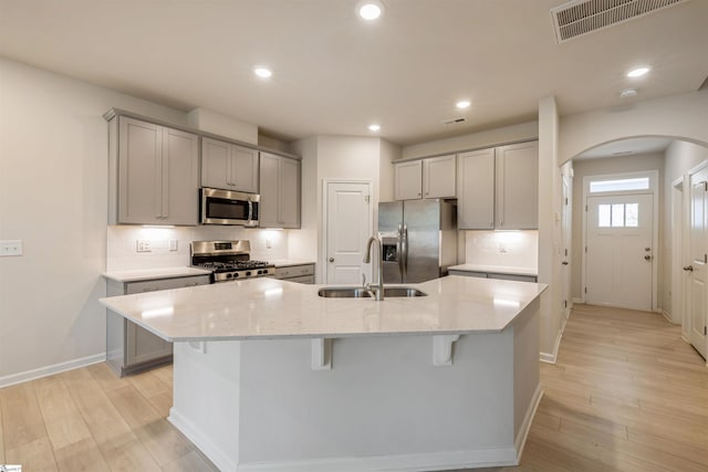 kitchen featuring decorative backsplash, light hardwood / wood-style flooring, an island with sink, light stone countertops, and stainless steel appliances