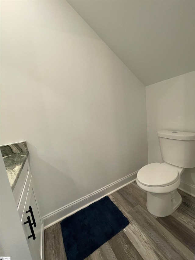 bathroom with hardwood / wood-style floors, toilet, vanity, and lofted ceiling