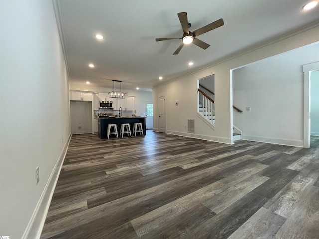 unfurnished living room with sink, ornamental molding, ceiling fan with notable chandelier, and dark hardwood / wood-style flooring