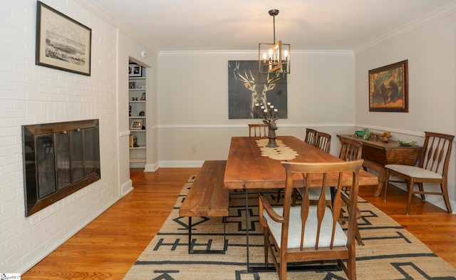 dining room featuring a chandelier, ornamental molding, brick wall, hardwood / wood-style flooring, and a brick fireplace