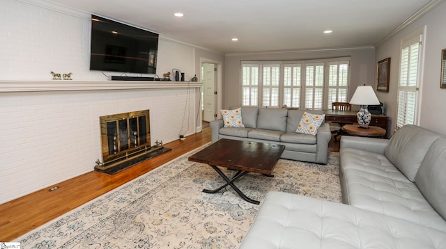 living room with wood-type flooring, ornamental molding, and a brick fireplace