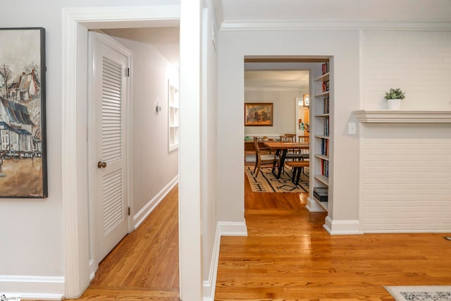 hallway featuring light hardwood / wood-style floors, crown molding, and built in shelves