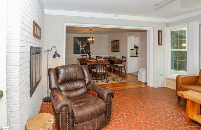 living room with a wealth of natural light, a notable chandelier, ornamental molding, wood-type flooring, and brick wall