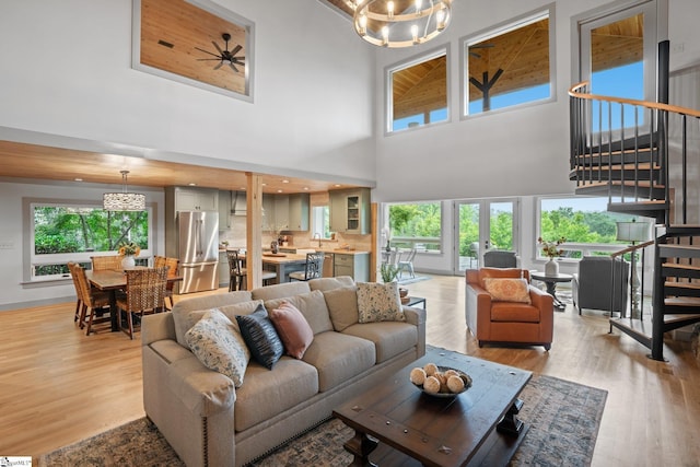 living room featuring ceiling fan with notable chandelier, light hardwood / wood-style floors, a high ceiling, and a wealth of natural light