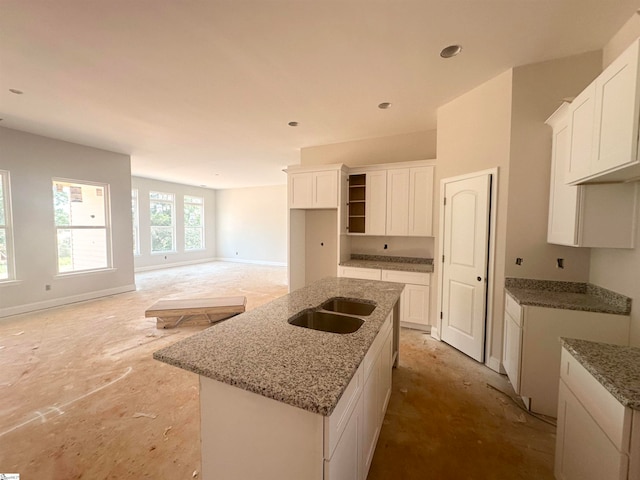 kitchen with white cabinetry, light stone countertops, sink, and a center island with sink