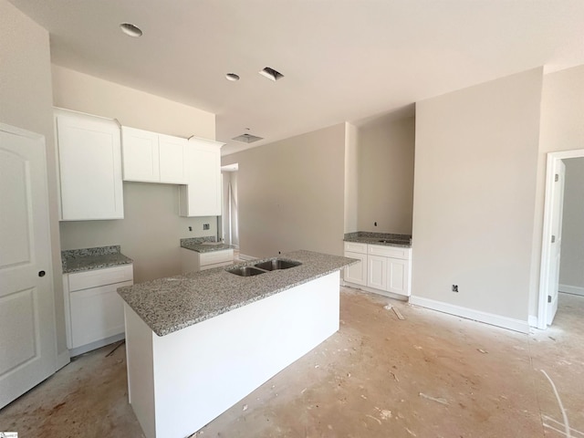 kitchen with white cabinets, a kitchen island with sink, sink, and light stone countertops