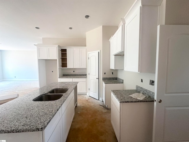 kitchen with white cabinetry, a kitchen island with sink, sink, and stone counters