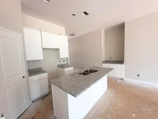 kitchen featuring a center island with sink, sink, white cabinetry, and stone counters