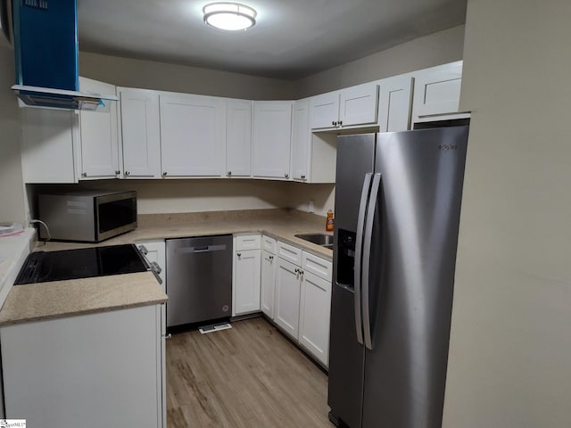 kitchen with light wood-type flooring, wall chimney exhaust hood, white cabinetry, light stone counters, and stainless steel appliances