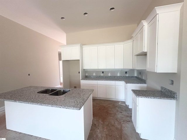 kitchen with white cabinets, stone counters, sink, and an island with sink