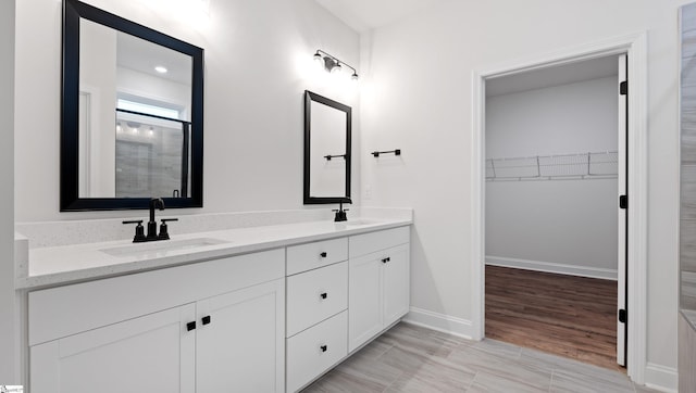 bathroom with a walk in closet, a sink, baseboards, and double vanity