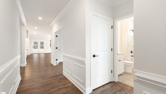 corridor with dark wood-style floors, a decorative wall, wainscoting, and crown molding