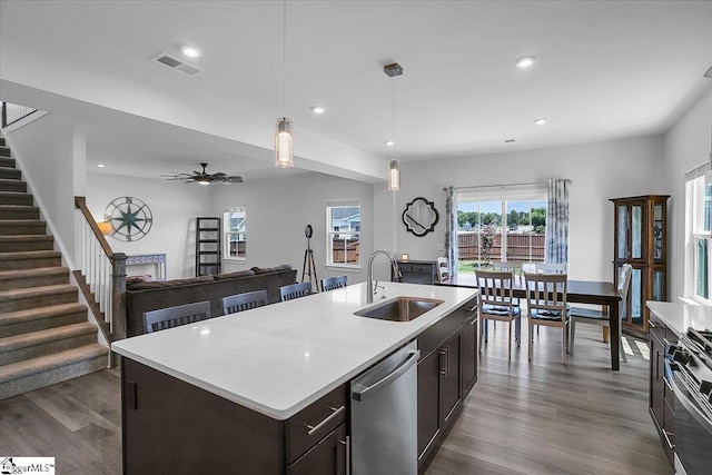 kitchen featuring sink, appliances with stainless steel finishes, hardwood / wood-style flooring, dark brown cabinetry, and a center island with sink