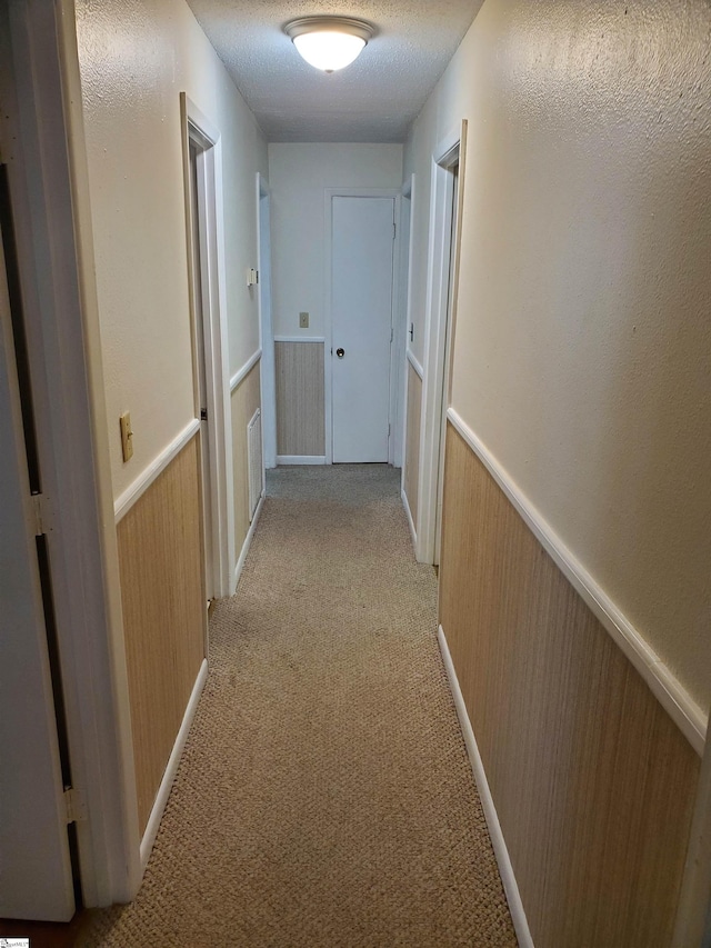 corridor with light colored carpet and a textured ceiling