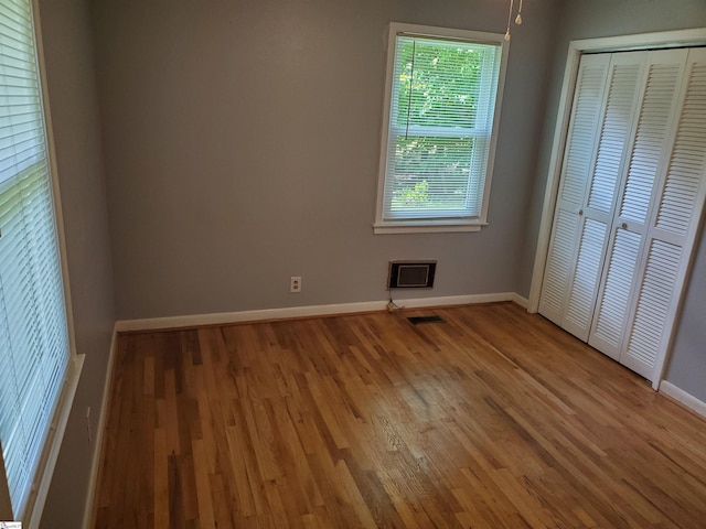 unfurnished bedroom featuring hardwood / wood-style flooring, a closet, and multiple windows