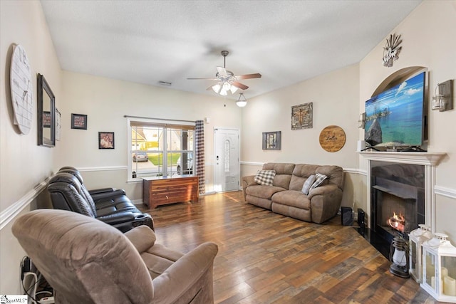 living room featuring ceiling fan, a textured ceiling, dark hardwood / wood-style floors, and a tiled fireplace