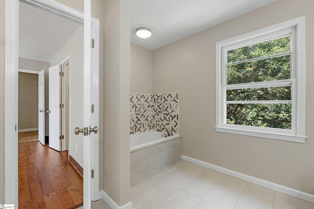 bathroom featuring a wealth of natural light, wood-type flooring, and tiled tub