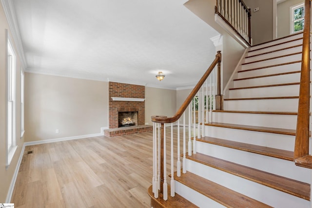 stairway featuring brick wall, crown molding, hardwood / wood-style floors, and a brick fireplace