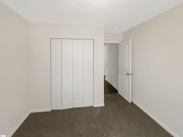 unfurnished bedroom featuring baseboards, dark colored carpet, and a closet