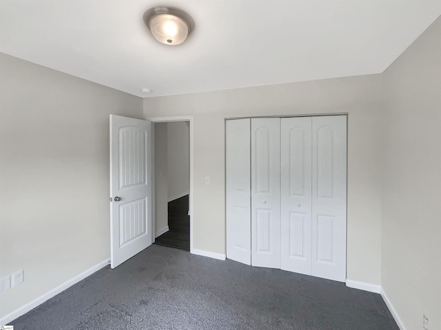 unfurnished bedroom featuring dark colored carpet, a closet, and baseboards