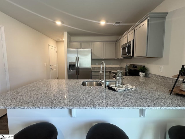 kitchen featuring appliances with stainless steel finishes, sink, light stone counters, gray cabinetry, and kitchen peninsula