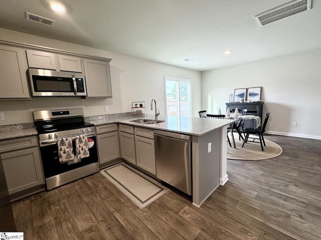 kitchen with appliances with stainless steel finishes, light stone counters, sink, dark hardwood / wood-style floors, and kitchen peninsula