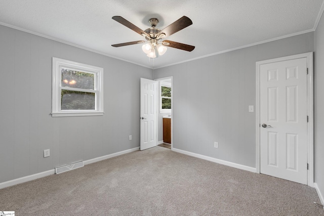 spare room featuring a textured ceiling, crown molding, carpet flooring, and ceiling fan