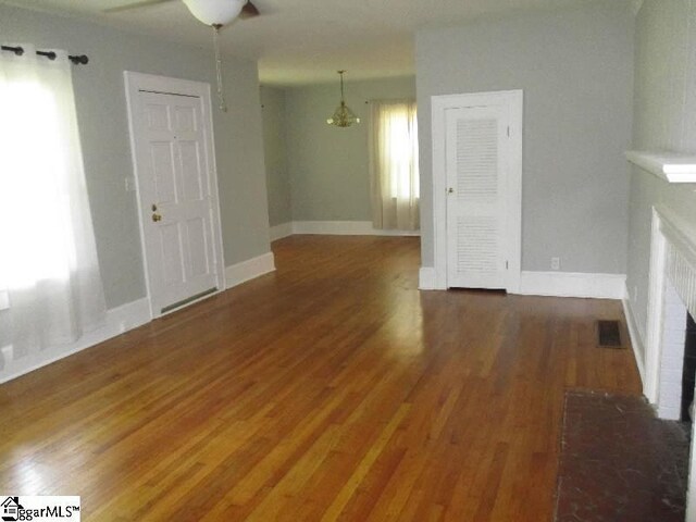 unfurnished living room with a fireplace, ceiling fan with notable chandelier, and wood-type flooring