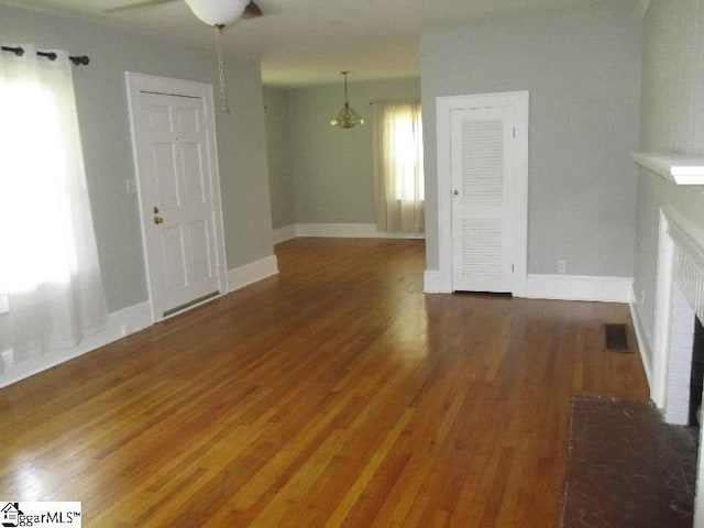 unfurnished living room with dark wood-type flooring, a brick fireplace, visible vents, and baseboards