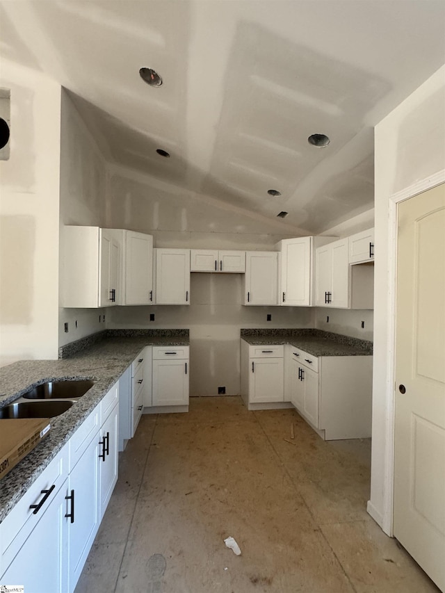 kitchen with white cabinetry, dark stone counters, sink, and vaulted ceiling