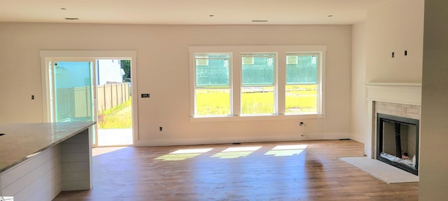 unfurnished living room featuring baseboards, a fireplace with flush hearth, and wood finished floors