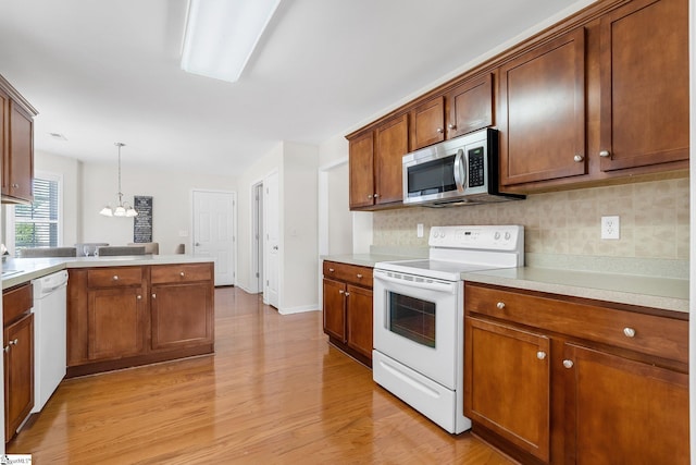 kitchen featuring light wood-type flooring, tasteful backsplash, decorative light fixtures, and white appliances