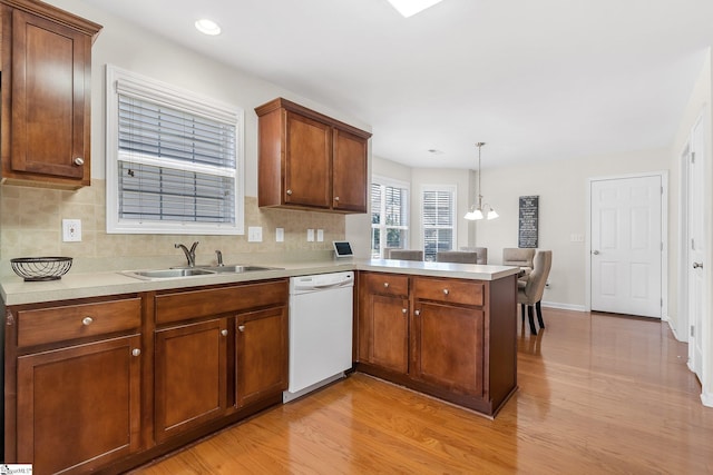 kitchen with sink, decorative light fixtures, light wood-type flooring, white dishwasher, and kitchen peninsula