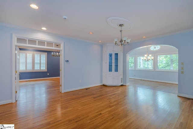 spare room featuring crown molding, light wood-style floors, arched walkways, and an inviting chandelier